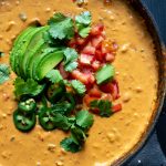 Chipotle Cashew Queso Dip topped with fresh tomato, cilantro, avocado and jalapeno served in a cast iron skillet.