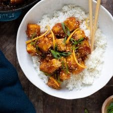 orange tofu chicken over white rice with chopsticks on wood table