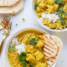 two bowls of yellow curry with naan bread over rice in white bowl