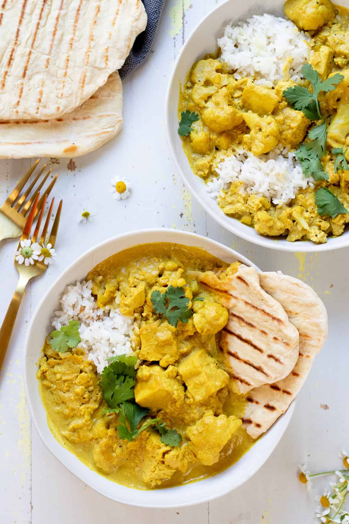 bowls of yellow curry with cauliflower and tofu with naan bread and cilantro