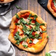 vegan flatbread margherita pizza on wood background with a glass of wine and fresh tomatoes