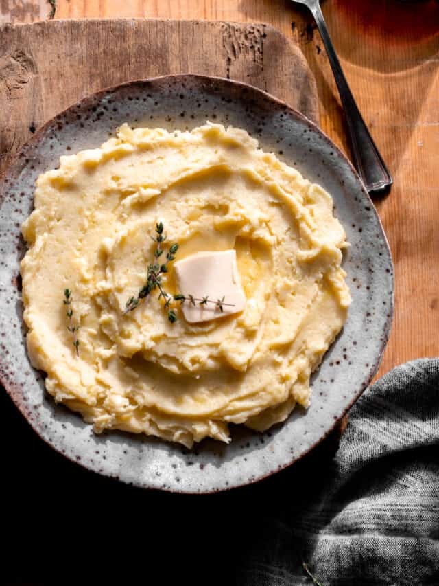 Mashed potatoes with pat of butter and fresh thyme styled in bowl.