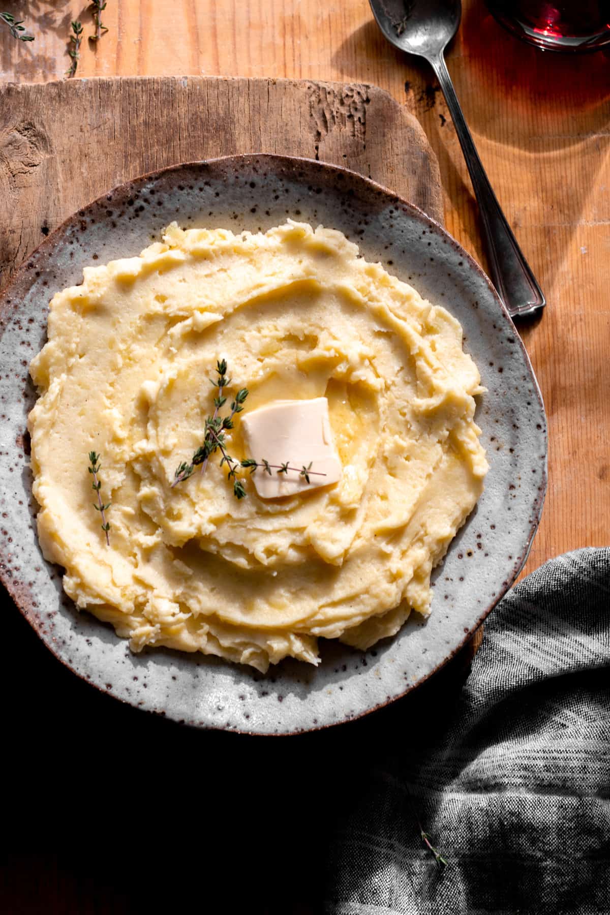 Mashed potatoes with pat of butter and fresh thyme styled in bowl.