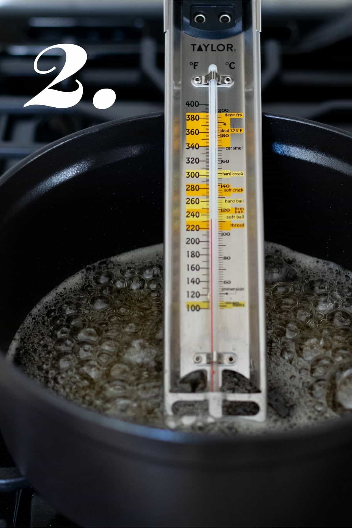 Sugar boiling on stove with candy thermometer reading temperature of sugar.