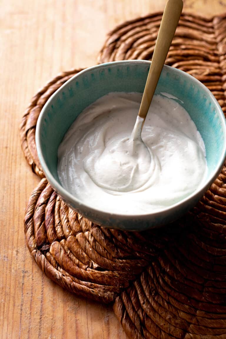 Vegan sour cream with gold spoon in blue bowl.