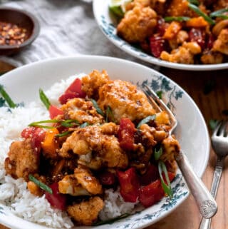 Cauliflower tossed in Kung Pao sauce served over white rice in white bowl.