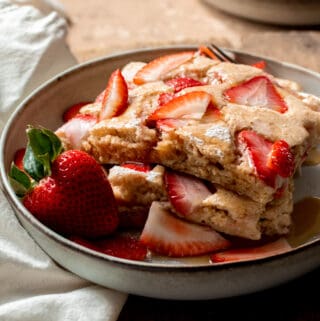 Three pancakes stacked on one another with strawberries on top in shallow bowl.