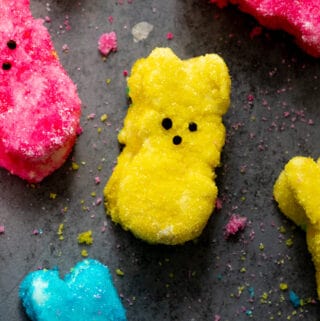 Yellow, pink, and blue peep marshmallows on dark surface.