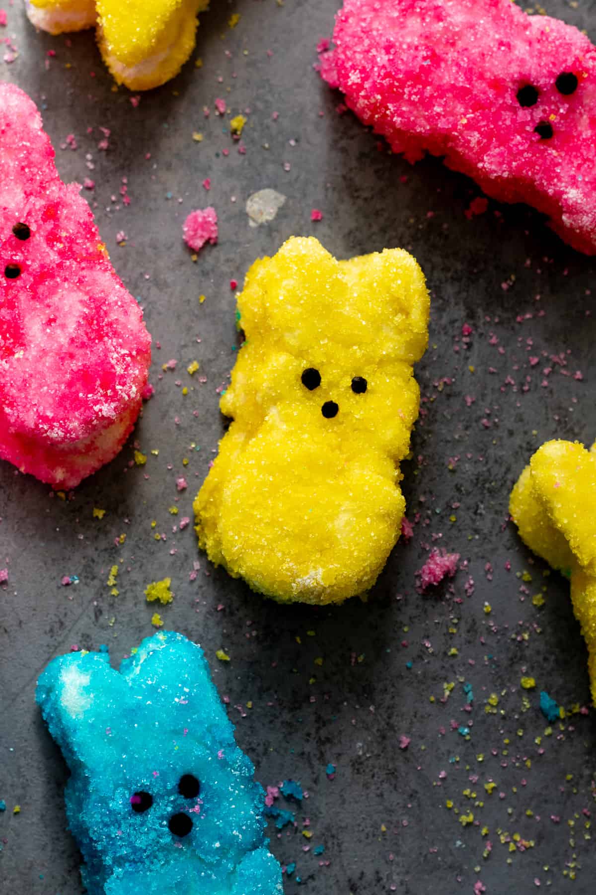 Yellow, pink, and blue peep marshmallows on dark surface.