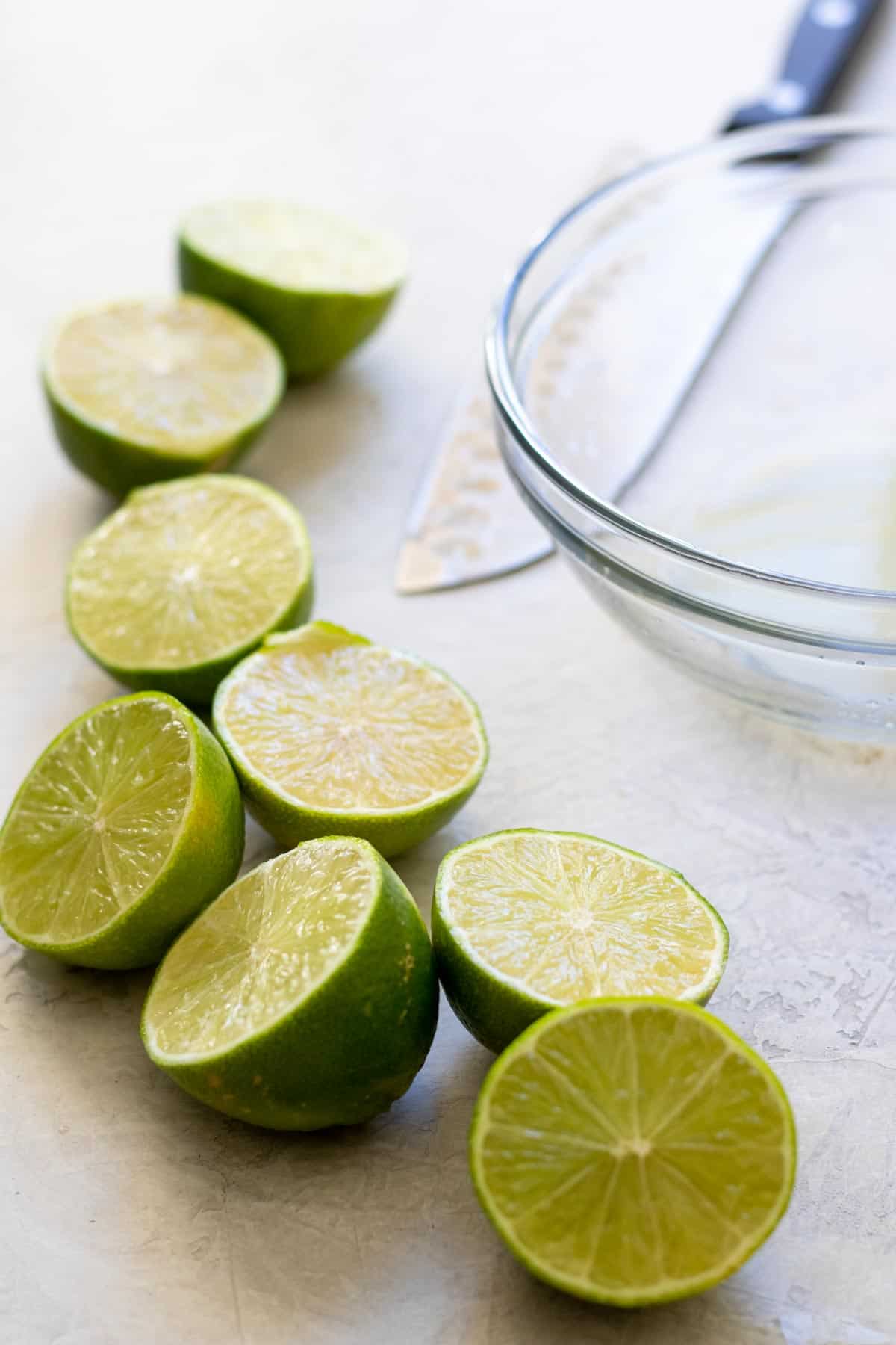 Limes cut in half near glass bowl with knife.