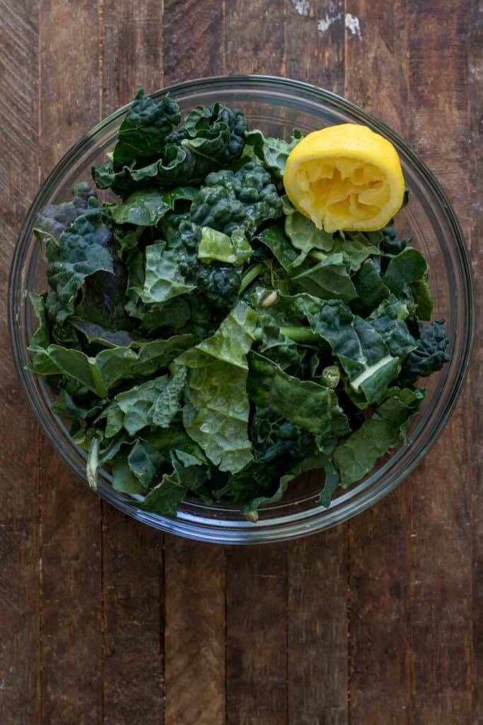 Kale in glass bowl on wooden table with lemon juice squeezed overtop.
