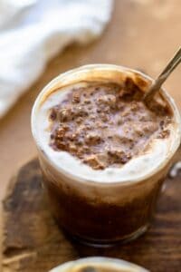 Mocha oats in glass with spoon on wooden surface.
