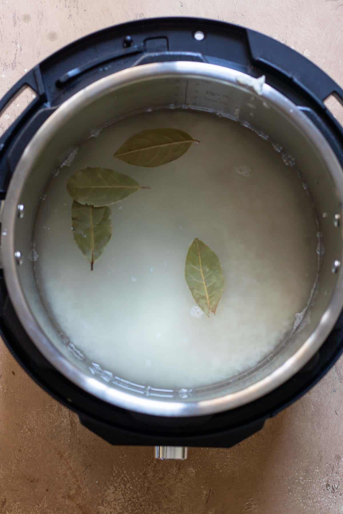 Water and bay leaves added over rice in Instant Pot.