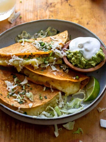 Three tacos served with shredded cabbage and sour cream and guacamole.