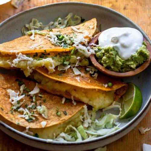 Three tacos served with shredded cabbage and sour cream and guacamole.