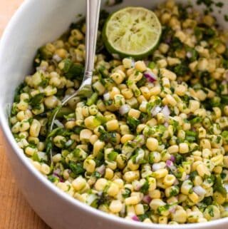 Corn salsa with half lime in large white bowl and silver spoon.