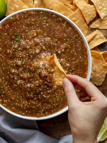 Salsa in white bowl with hand dipping chip in.