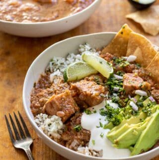 Stew topped with sour cream, avocado slices, corn chips over cilantro rice in white bowl.