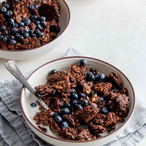 Two bowls of granola with milk and berries on blue napkin.