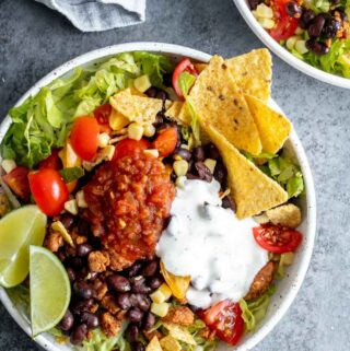 Taco salad bowl garnished with salsa and lime wedges in white bowl.