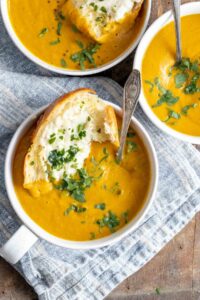 3 bowls of pumpkin soup garnished with parsley and garlic bread dipped in.