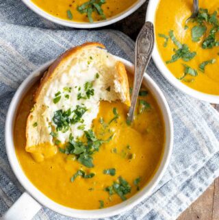 3 bowls of pumpkin soup garnished with parsley and garlic bread dipped in.