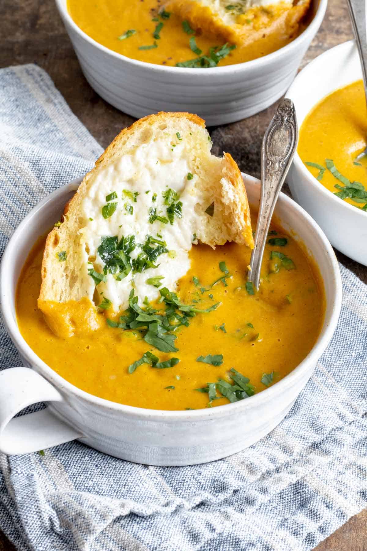 Pumpkin soup in bowl garnished with parsley and garlic bread dipped in.