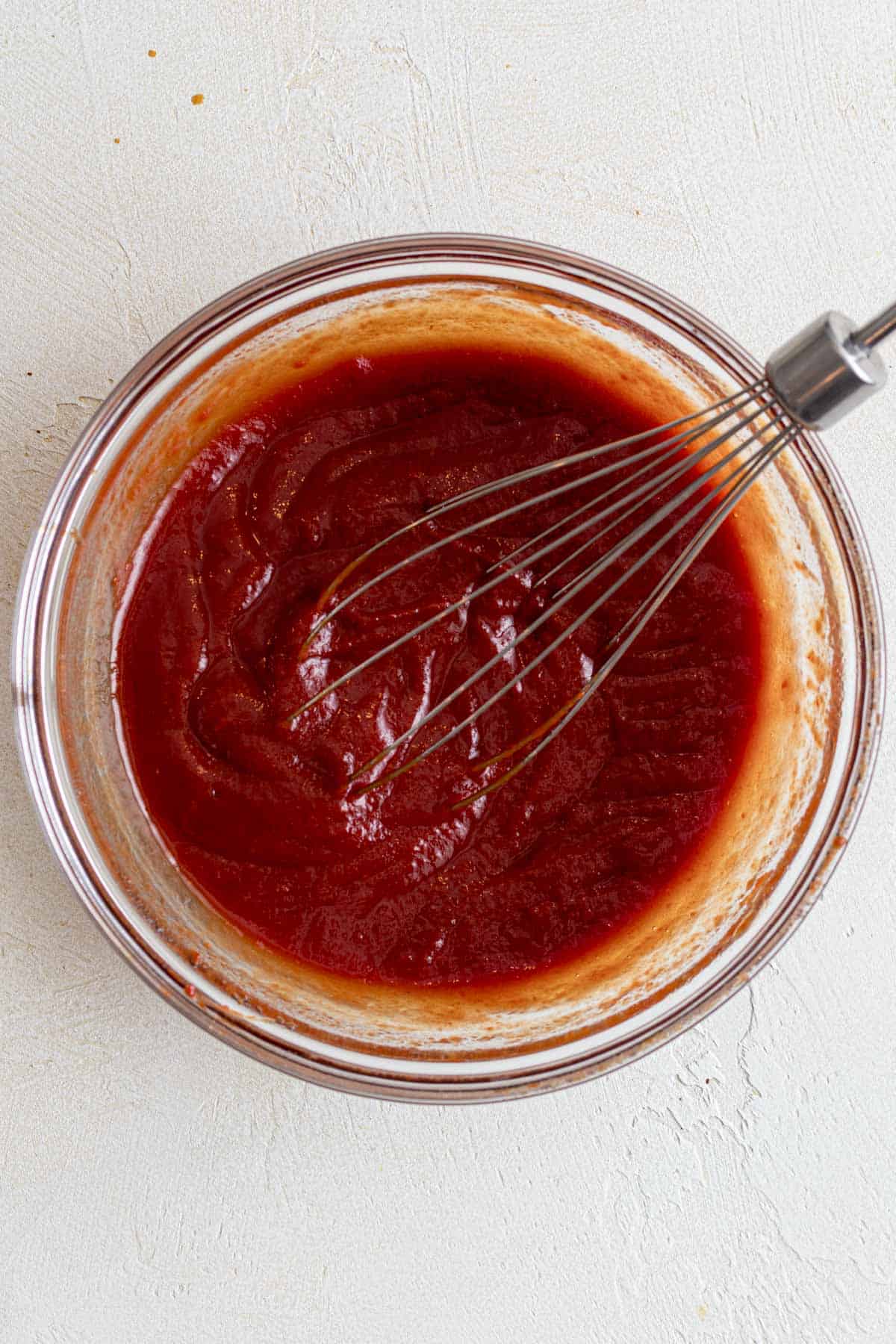 Tomato paste, maple syrup, apple cider vinegar, and tamari whisked together into ketchup in a glass mixing bowl.