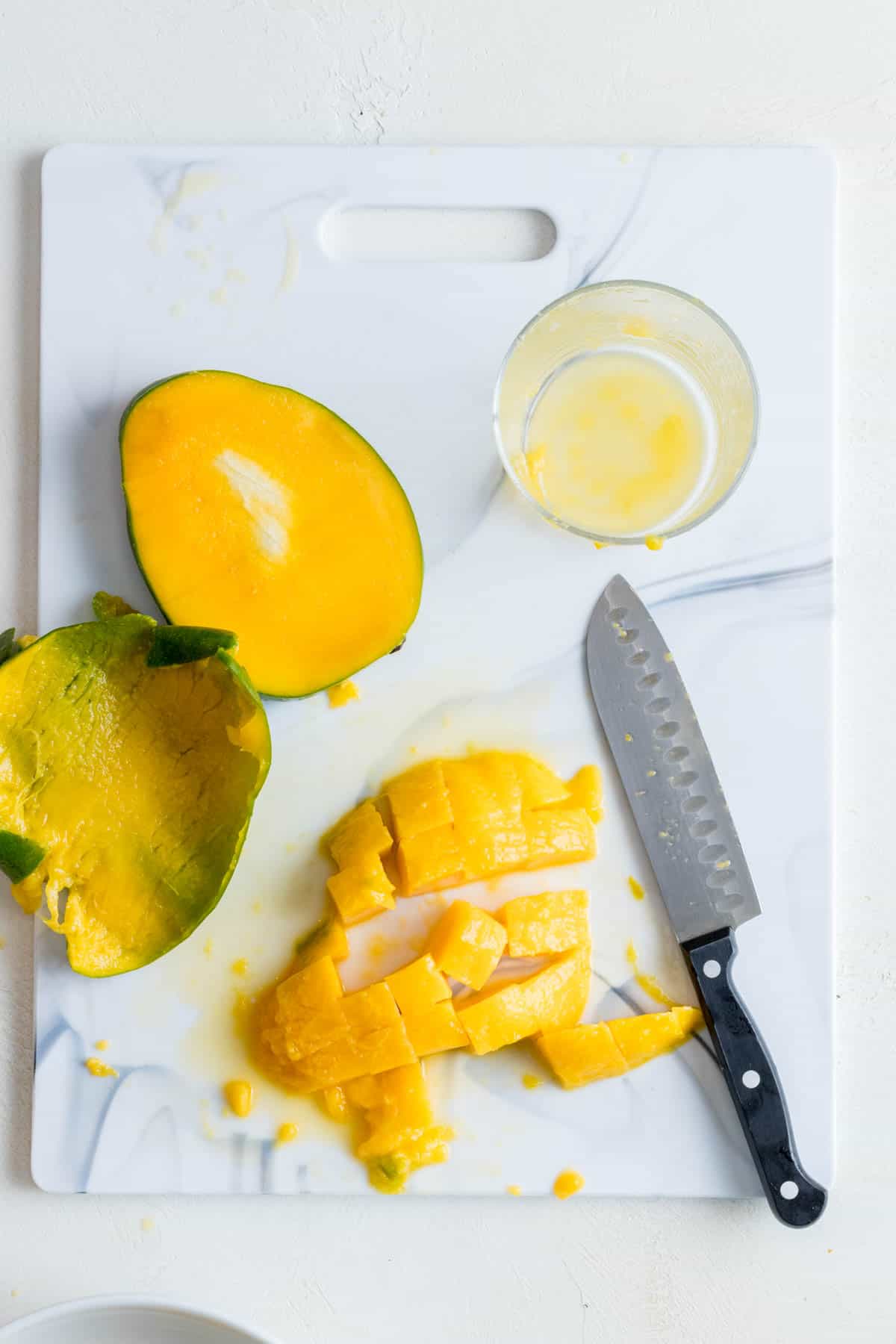 Diced mango half on white cutting board.