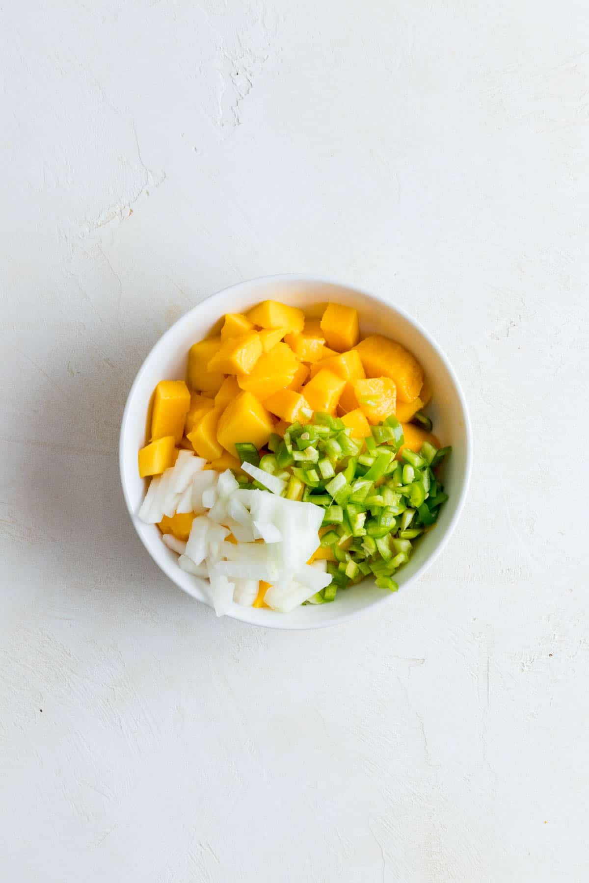 Mango, peppers, and onion in white bowl.
