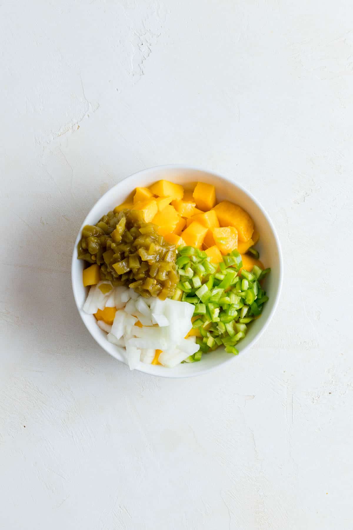 Mango, anaheim pepper, onion, and green chilies in a bowl.