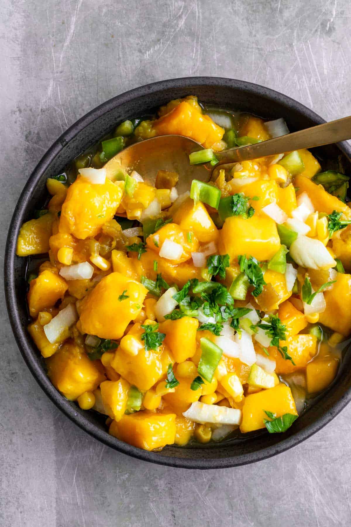 Mango corn salsa with gold spoon in black bowl.