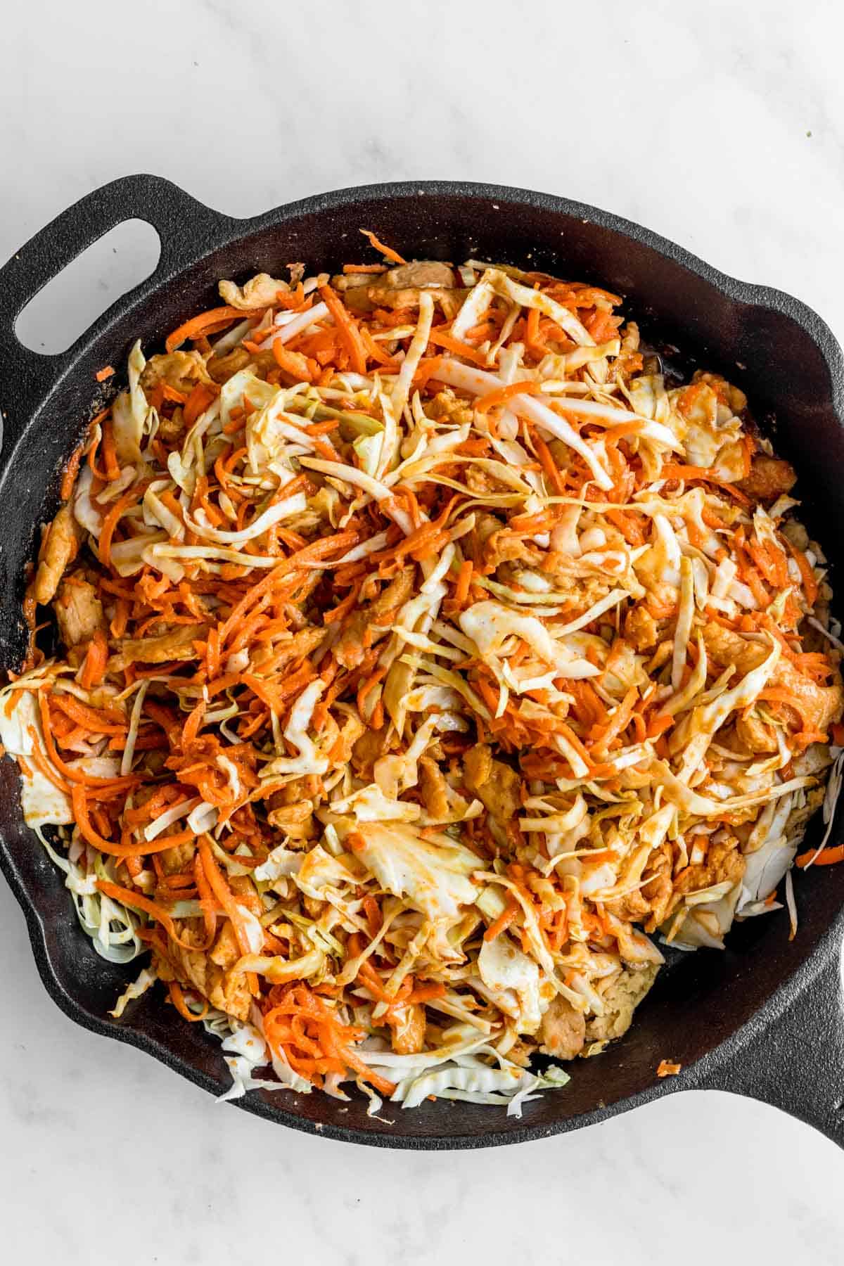 Shredded carrot, cabbage and soy curls tossed in peanut sauce in cast iron skillet.