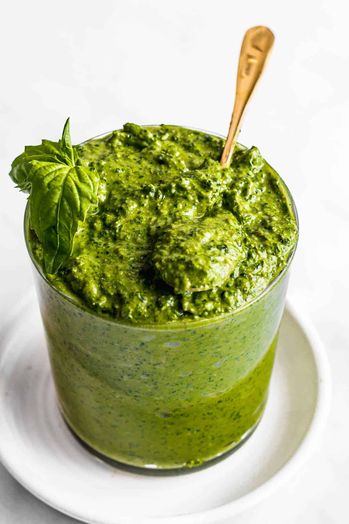 Vegan pesto in glass jar with gold spoon garnished with fresh basil.