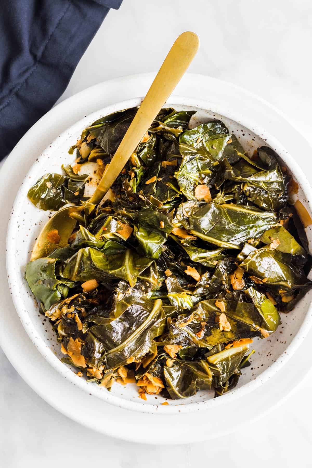 Collard greens in white bowl with gold spoon.