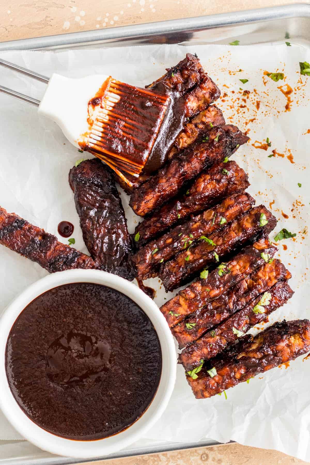 Tempeh strips on parchment paper with a side of BBQ sauce.