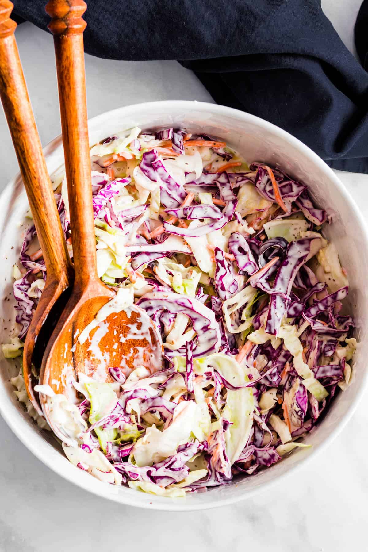 Coleslaw in serving bowl with blue tea towel with white background.