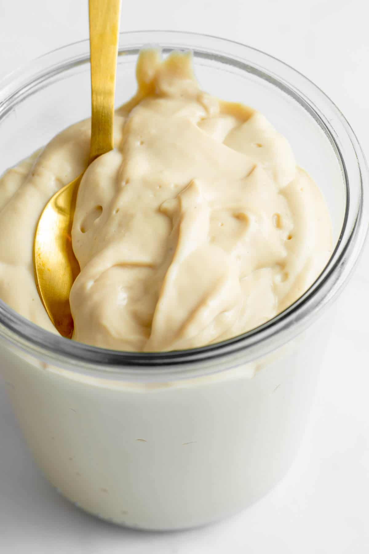 Mozzarella cheese sauce in glass storage jar with gold spoon.