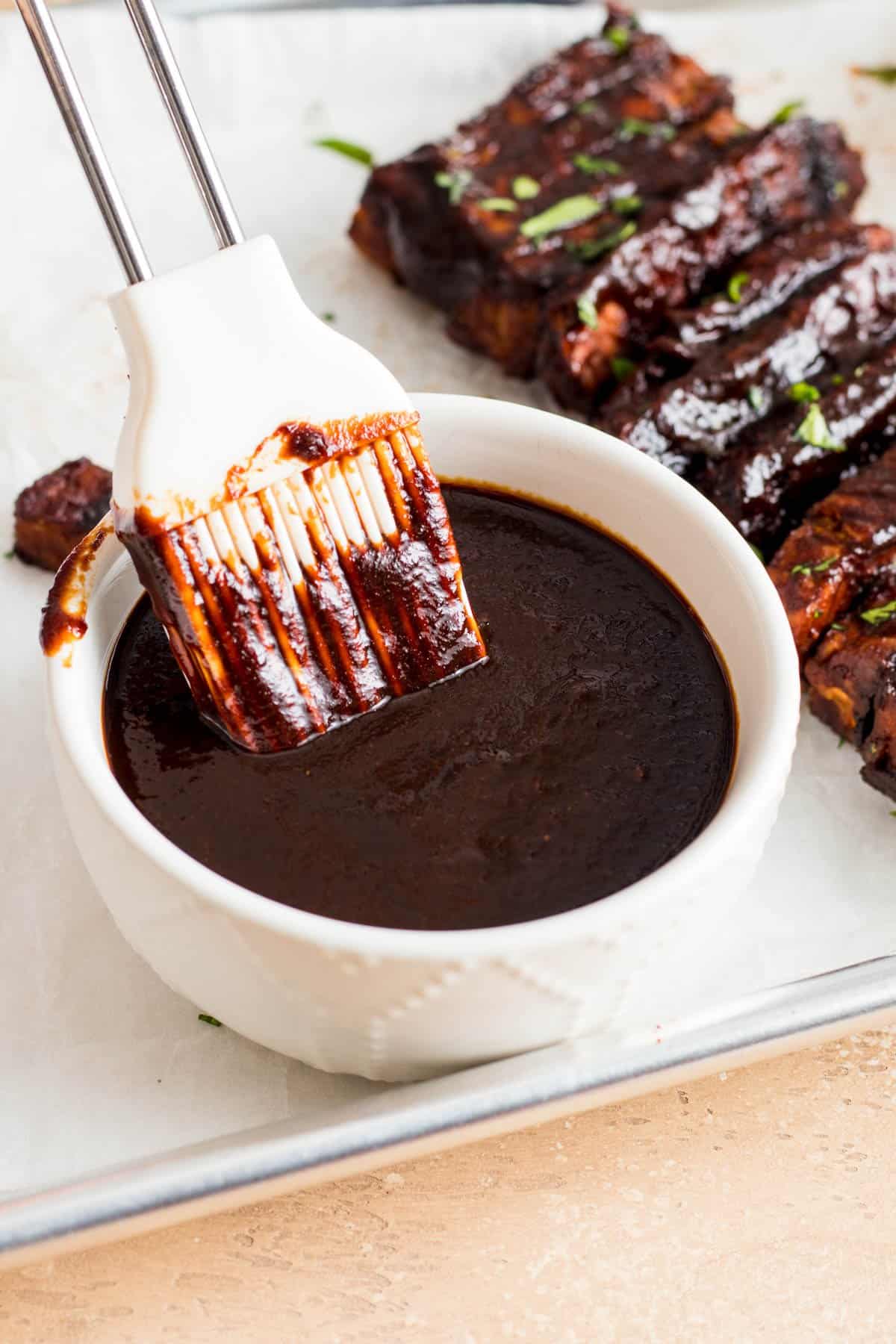 BBQ sauce in a white bowl with a silicone brush dipped in.