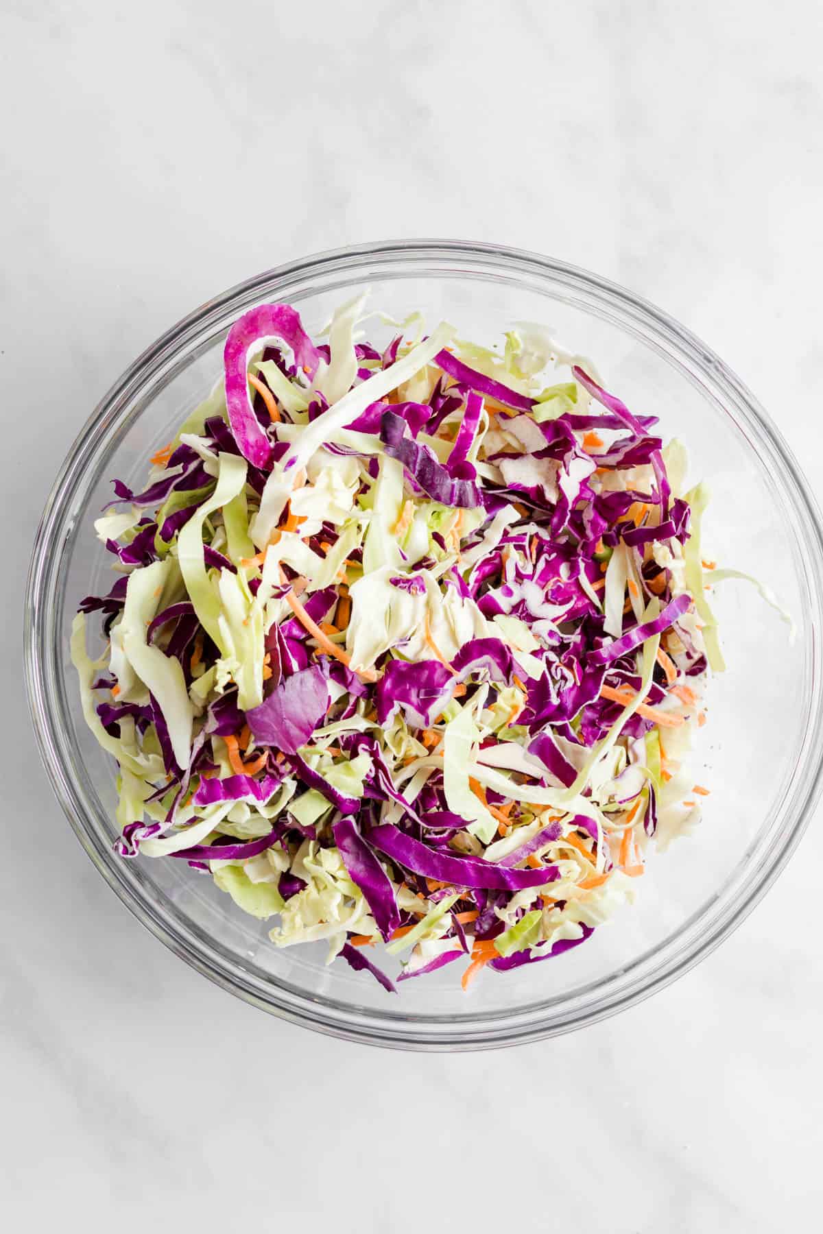 Shredded cabbage and carrots mix added into bowl with dressing.
