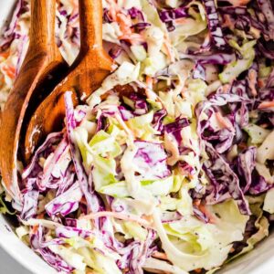Vegan coleslaw with shredded cabbage in white bowl with wood serving utensils.