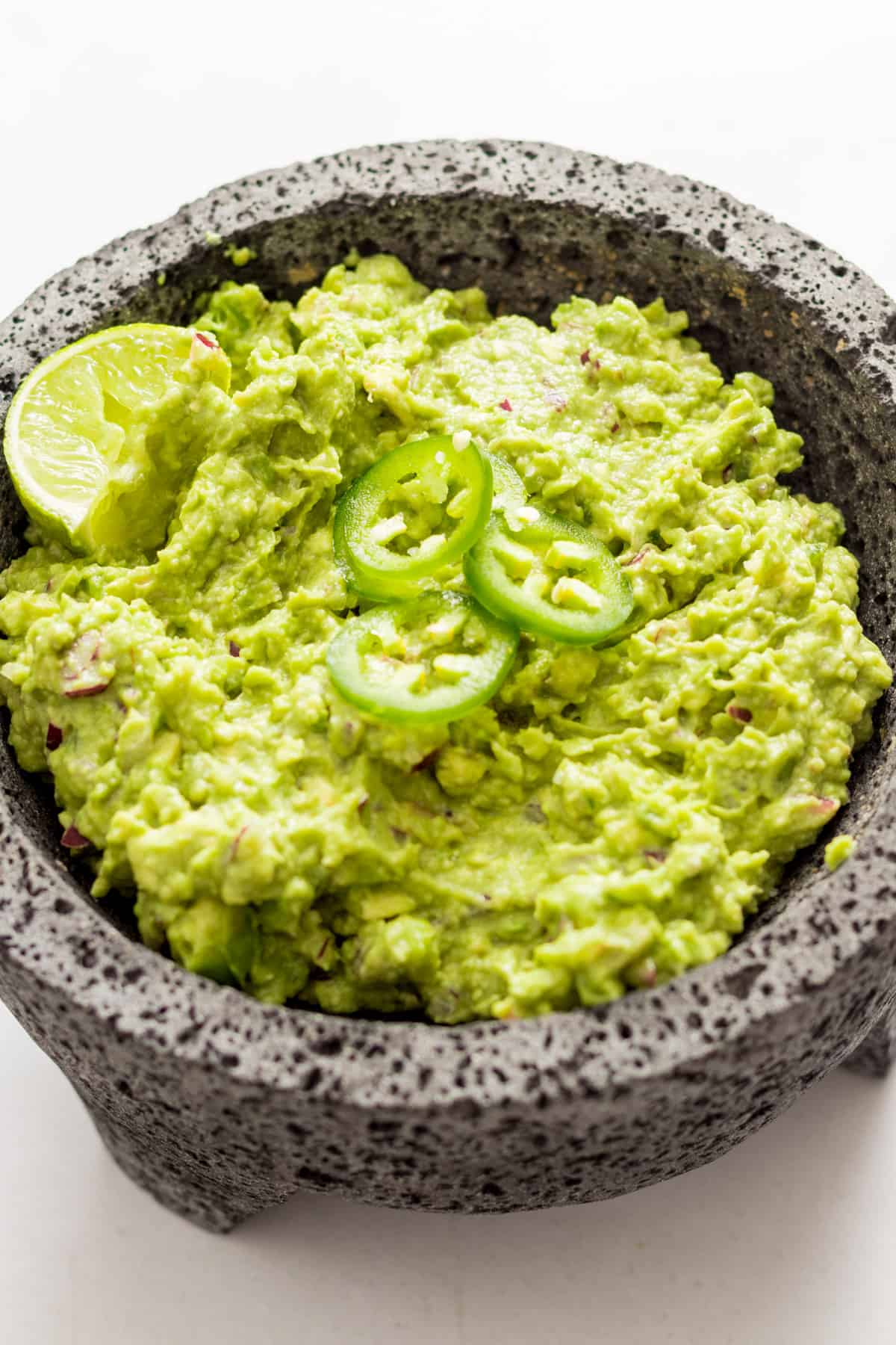 Guacamole in a molcajete garnished with jalapenos and lime.
