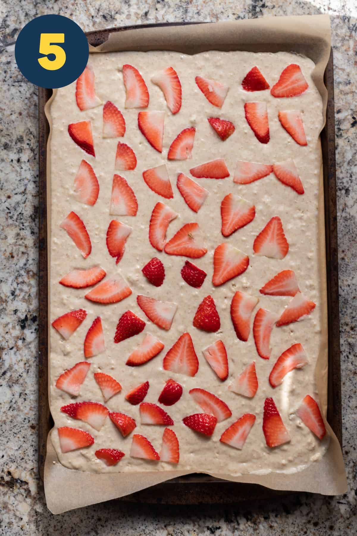 Pancake mix spread in baking sheet and topped with sliced strawberries before baking.
