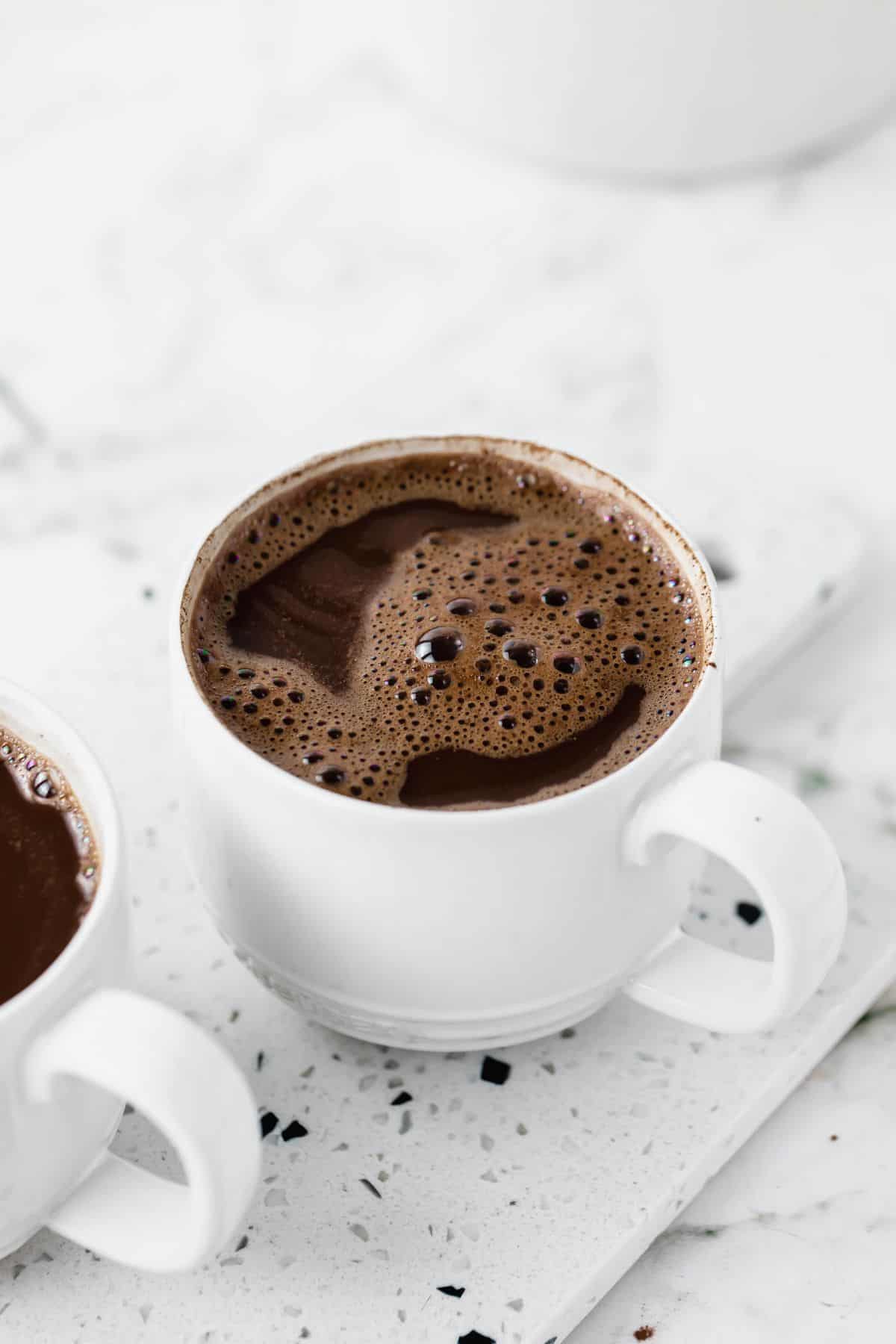 Mug full of hot chocolate on white surface.