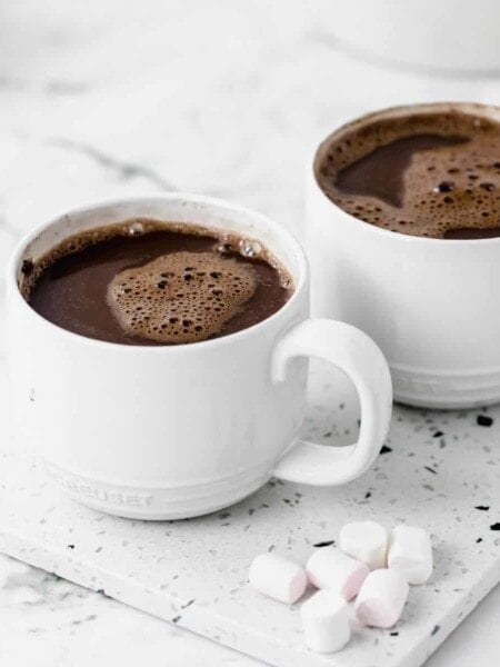 Two white mugs of cocoa by marshmallows.