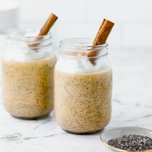 Two jars of chia pudding with coconut whip and cinnamon sticks.