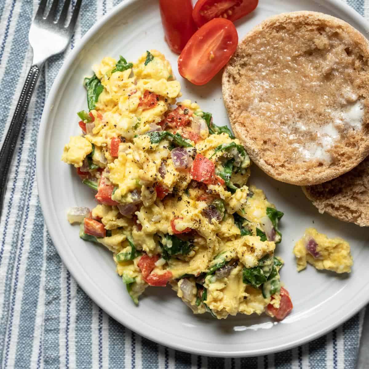 Vegan breakfast scramble on plate with english muffin and tomatoes.