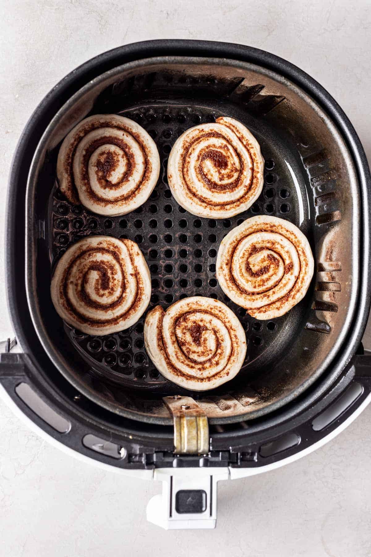 Air fryer basket with 5 cinnamon rolls in the bottom.