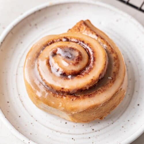 Cinnamon roll with icing on white plate.