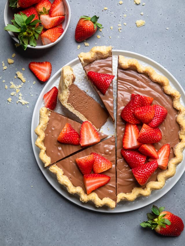 Pie garnished with strawberries and half of pie cut into slices.